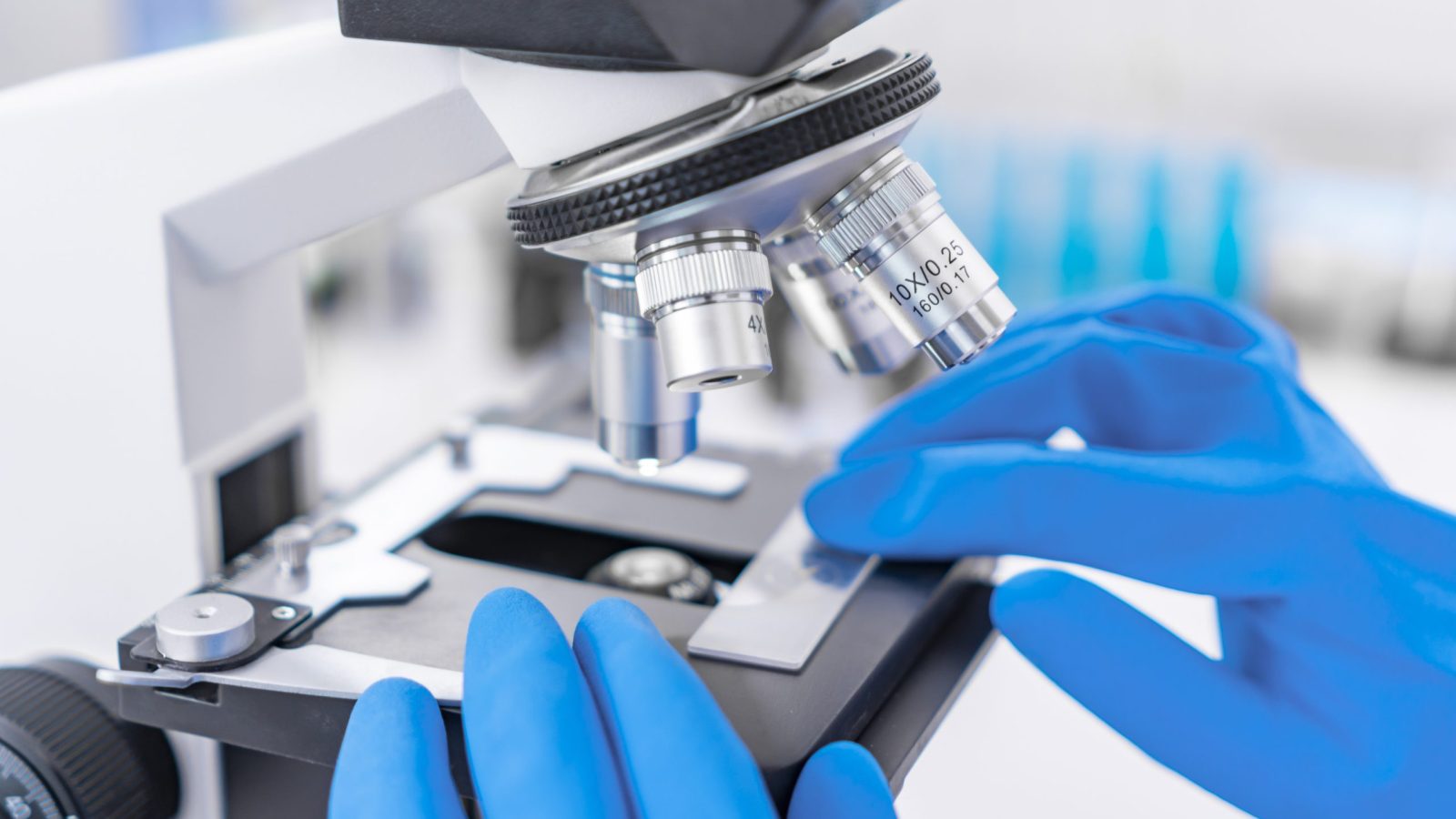 Scientist analyzing microscope slide at laboratory. Young woman technician is examining a histological sample, a biopsy in the laboratory of cancer research